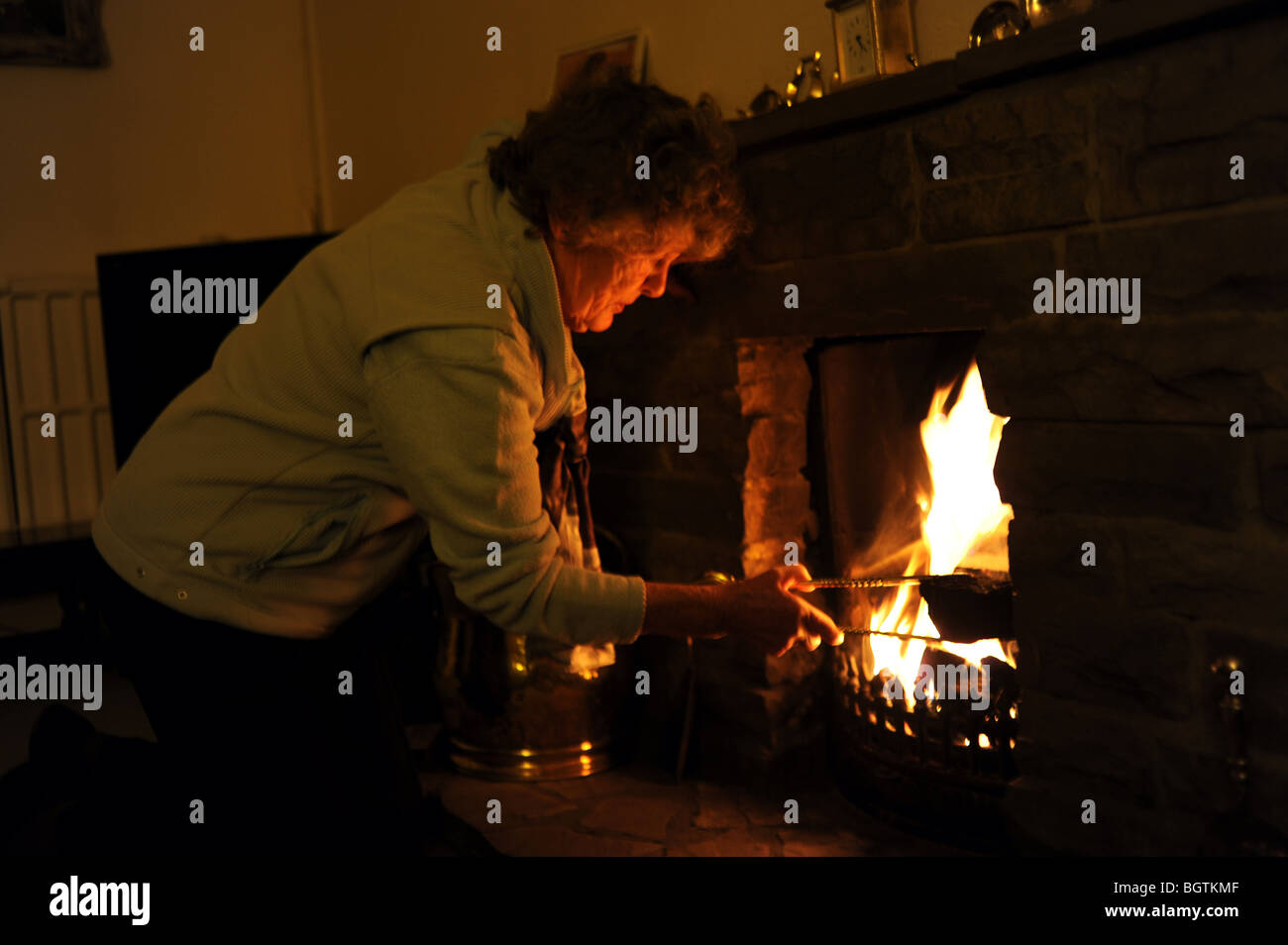Una pensionista hembra enciende un fuego abierto para mantenerse caliente en su casa mientras intenta ahorrar en las facturas de gas y electricidad del Reino Unido Foto de stock