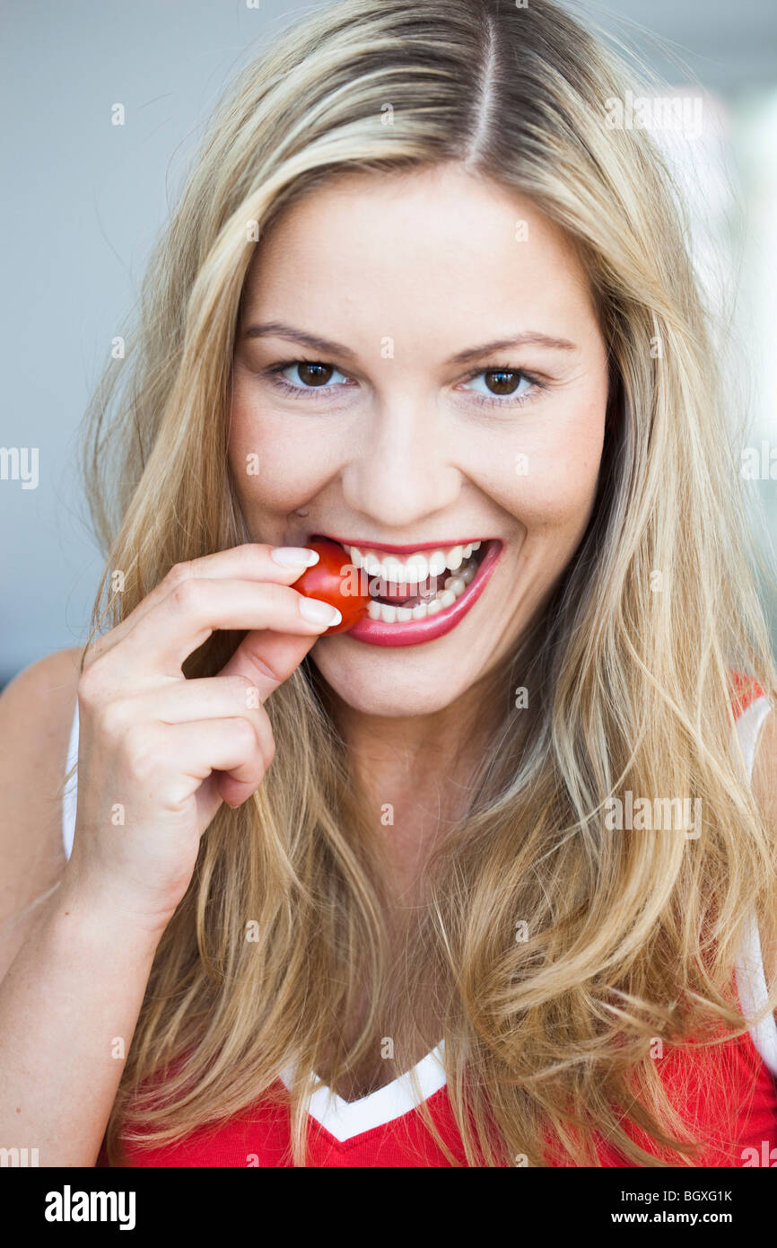 Mujer joven nibbling sobre tomate Foto de stock