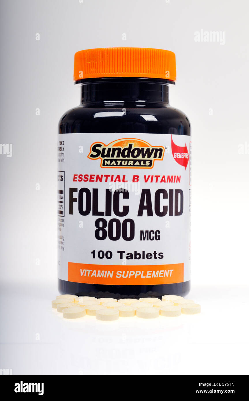 Un frasco cerrado cerrado de Sundown Naturals ácido fólico vitaminas con algunas píldoras derramado sobre fondo blanco. Foto de stock