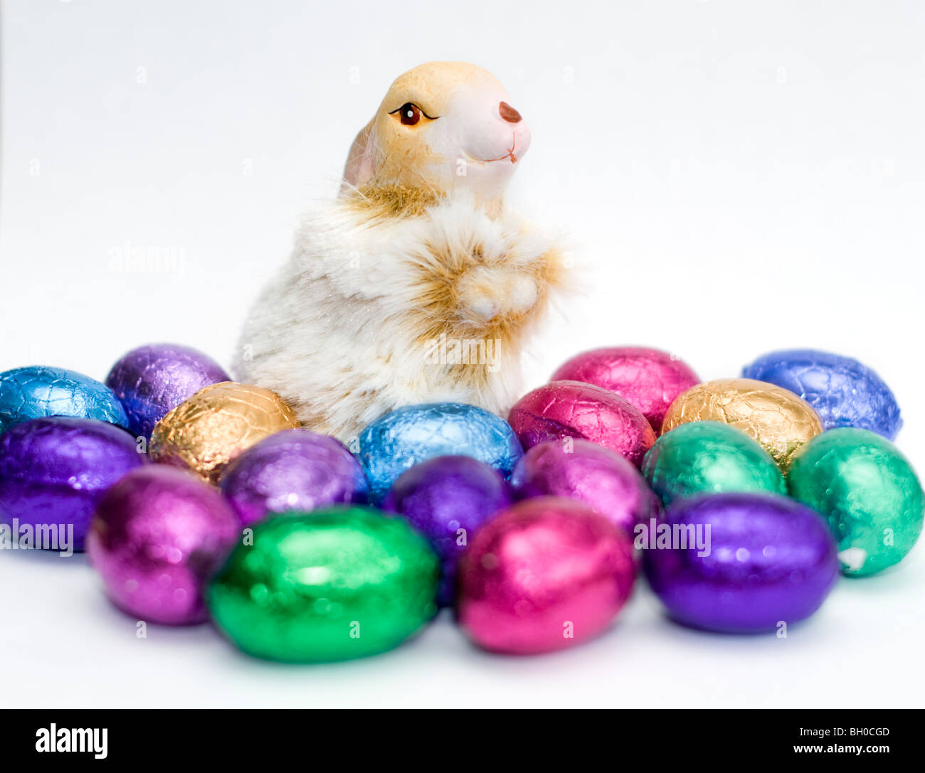 Ornamento De Un conejo rodeado de coloridos mini huevos de Pascua de chocolate sobre un fondo blanco. Foto de stock