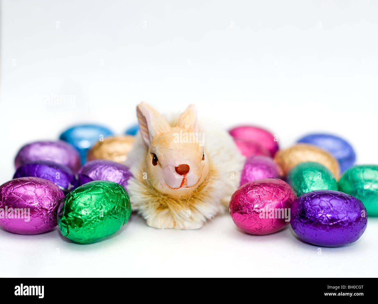 Ornamento De Un conejo rodeado por una selección de coloridos mini huevos de Pascua de chocolate sobre un fondo blanco. Foto de stock