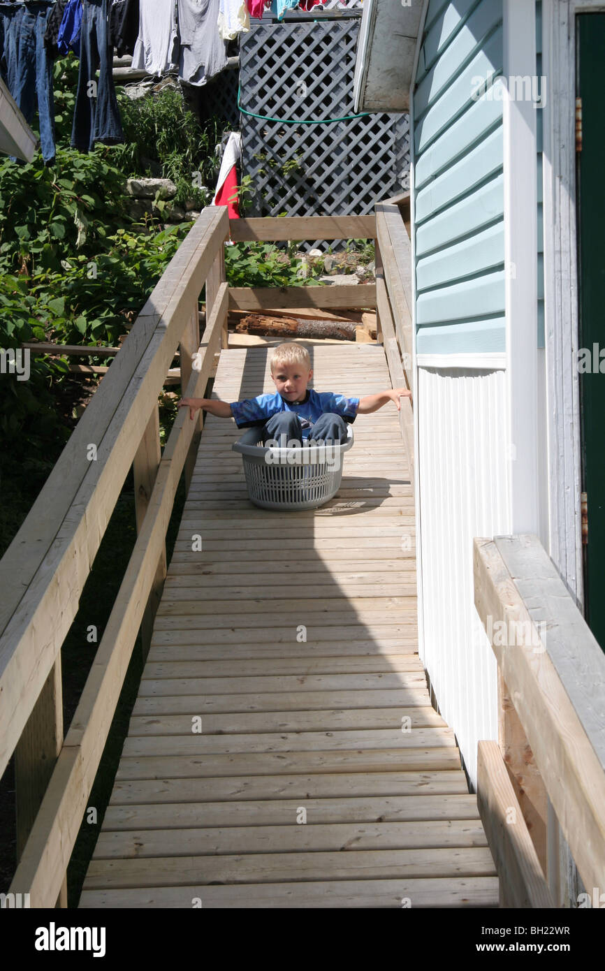 Para el entretenimiento un joven utiliza una cesta de lavandería como un trineo en el puerto de desembarco villa de Río Grey, Terranova Foto de stock