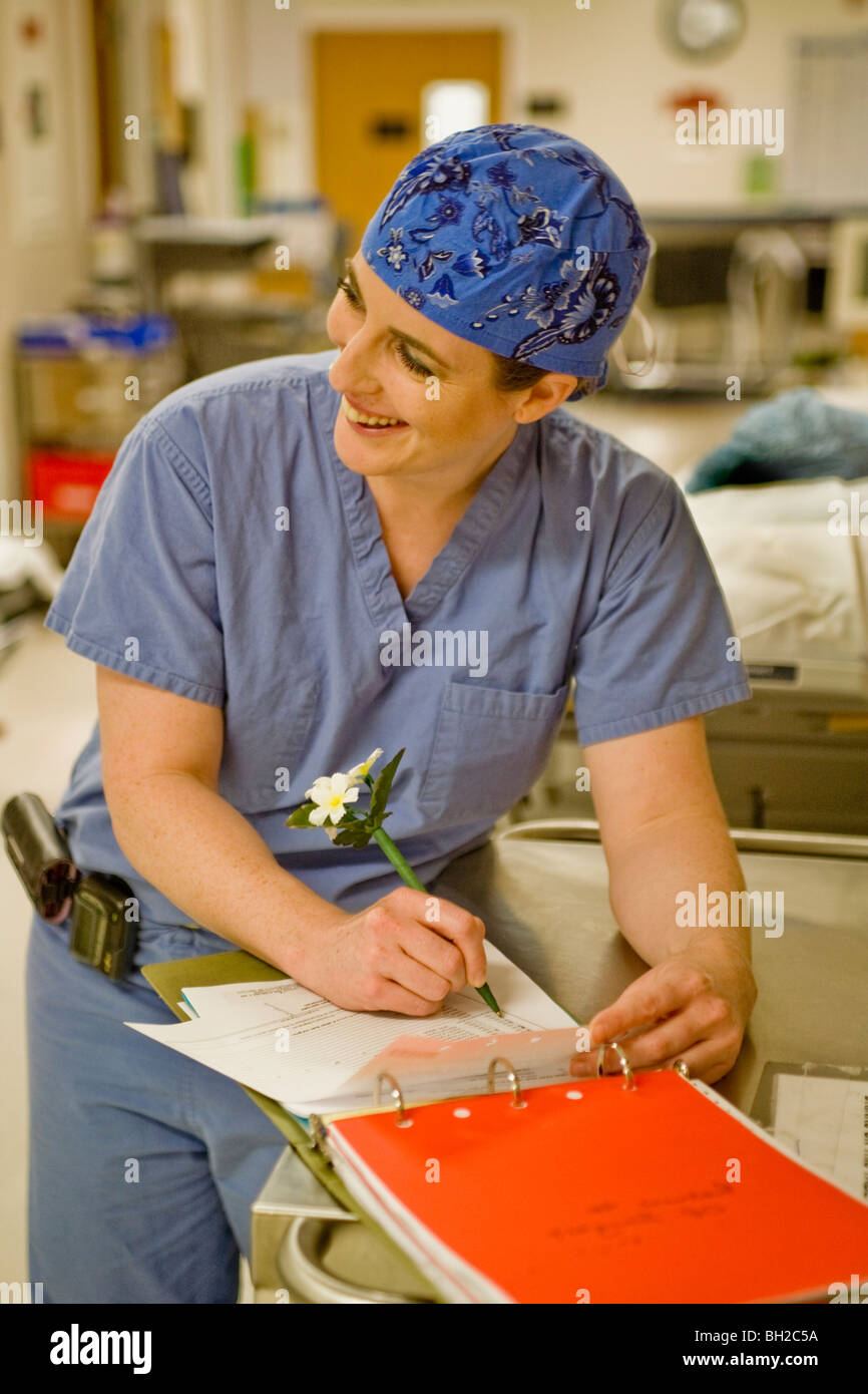 Vestida de 'scrubs', una mujer cirujano rellena el papeleo requerido legalmente con un decorado con motivos florales con lápiz antes de una operación en un S Foto de stock