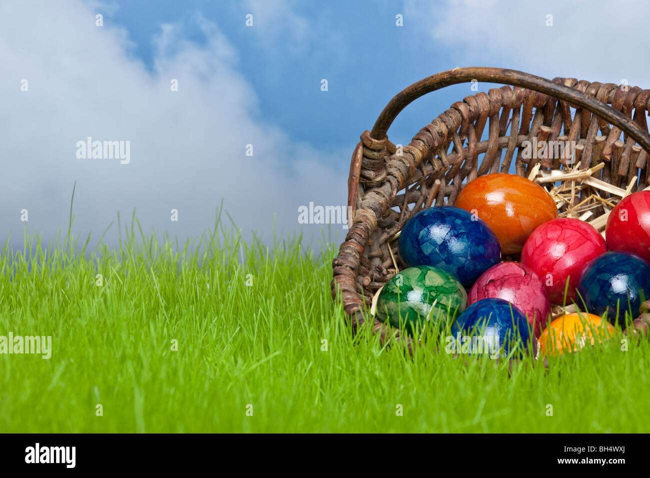 Los huevos de pascua en una cesta en la pradera con el cielo de fondo Foto de stock