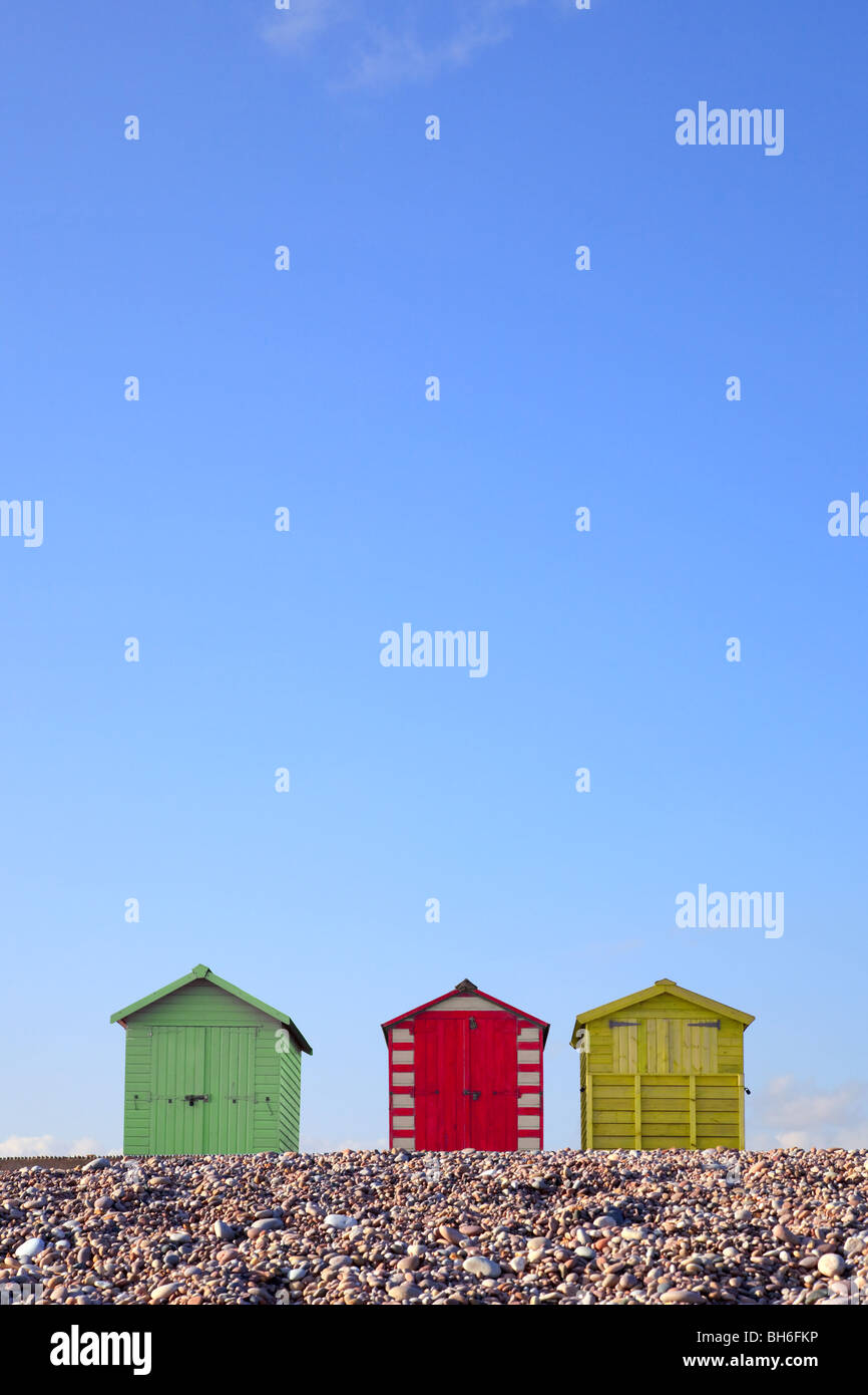 Tres coloridas casetas de playa contra un cielo azul brillante, ideada para permitir copia el espacio en la parte superior de la imagen. Foto de stock