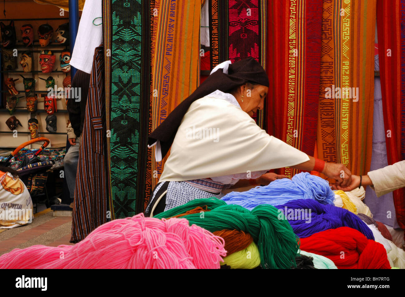 Ecuador, Otavalo, vista de un mercado callejero con una anciana indígena vestida con ropa local, vendiendo sus telas y otros h Foto de stock