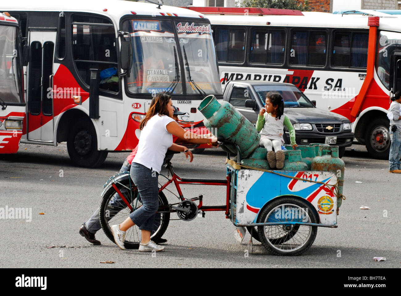 Ecuador, Otavalo, mujeres jóvenes empujando un triciclo lleno de cilindro de  gas mientras que una chica sentada con autobuses estacionados Fotografía de  stock - Alamy