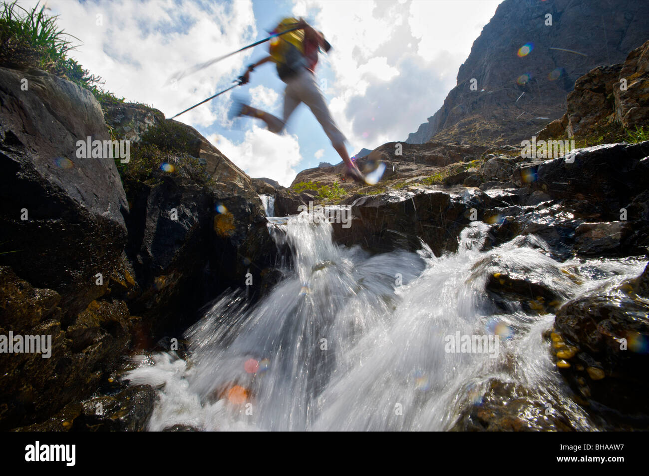 Caminante salta por encima de un riachuelo en el Williwaw Lagos Trail en Chugach State Park, cerca de Anchorage, Alaska, Southcentral Verano Foto de stock