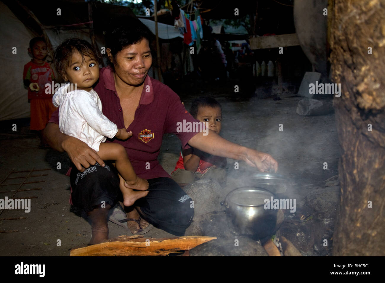 Hogar de la madre con el bebé prepara el desayuno sobre fuego abierto para su familia hacinados en campamentos de personas desplazadas de PDI en la oscuridad Foto de stock