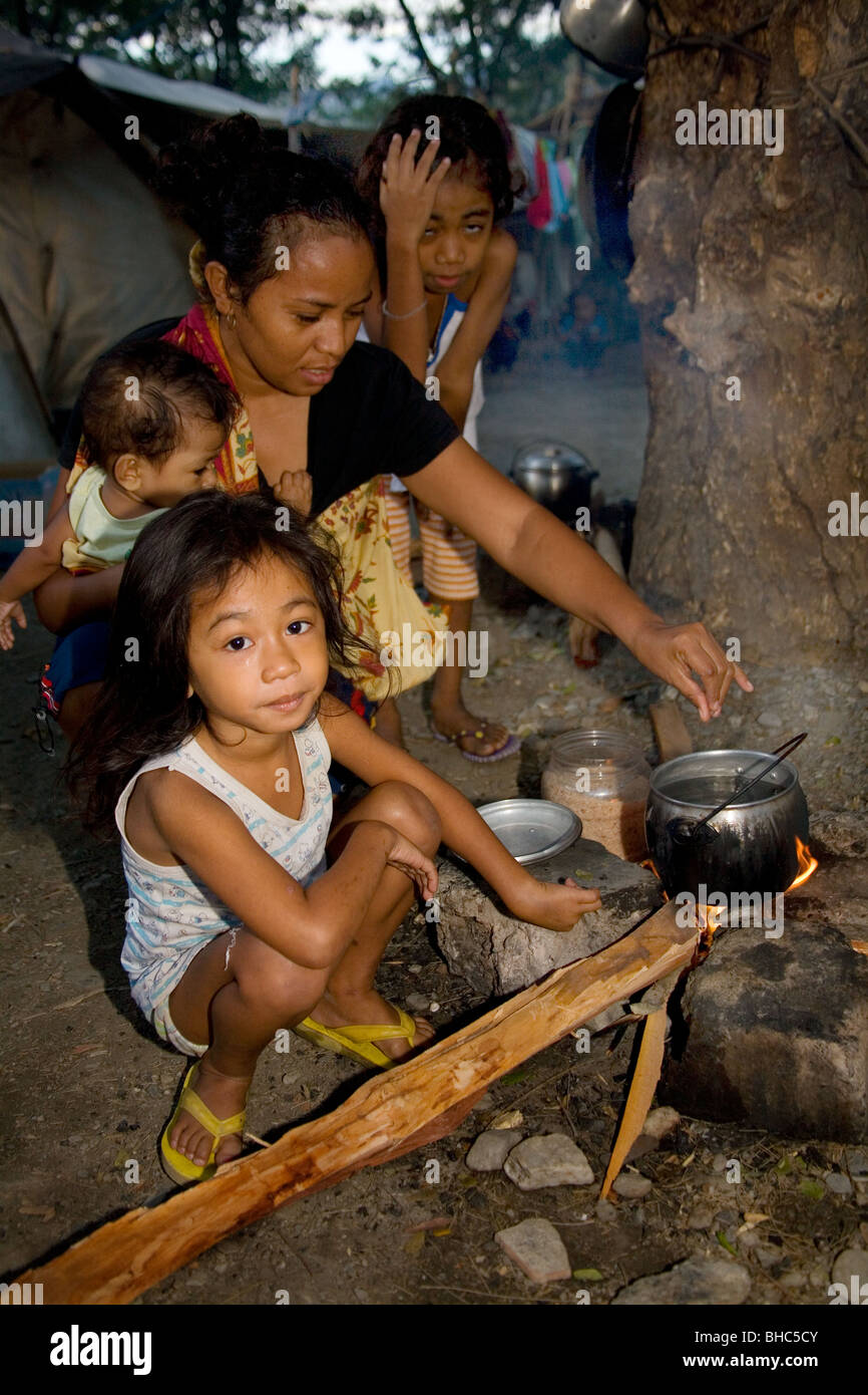 Familia con olla a fuego abierto a preparar el desayuno en el campamento para desplazados de IDP abarrotado de familias sin hogar en Dili, Timor Oriental Foto de stock
