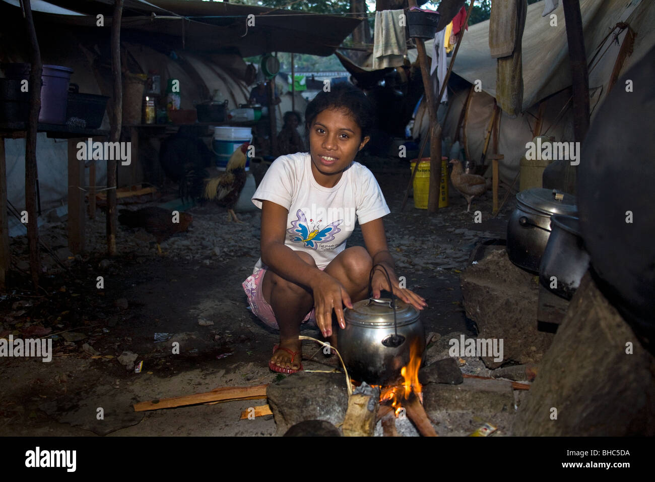 Mujer joven con olla a fuego abierto prepara una comida en el campamento para desplazados de IDP abarrotado de familias sin hogar en Dili, Timor Oriental Foto de stock