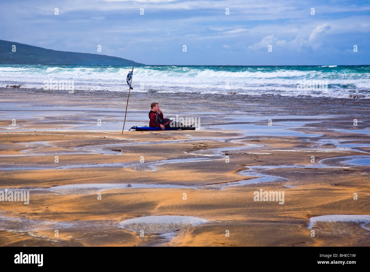 Hombre descansando sobre su tabla de surf en la playa de Fanore, County Clare, Irlanda. Foto de stock