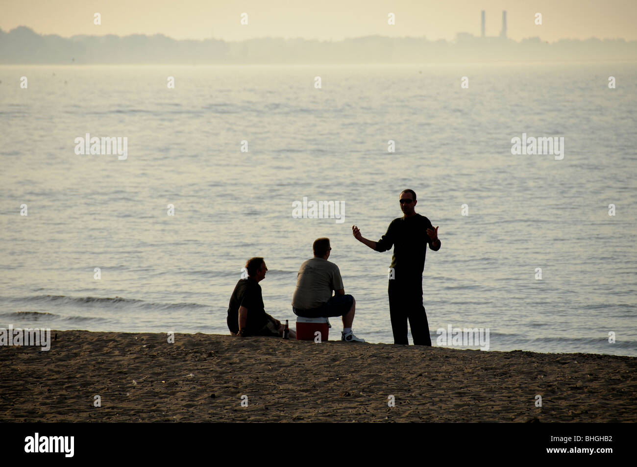 Tres hombres en animada conversación sobre la orilla del lago. Foto de stock