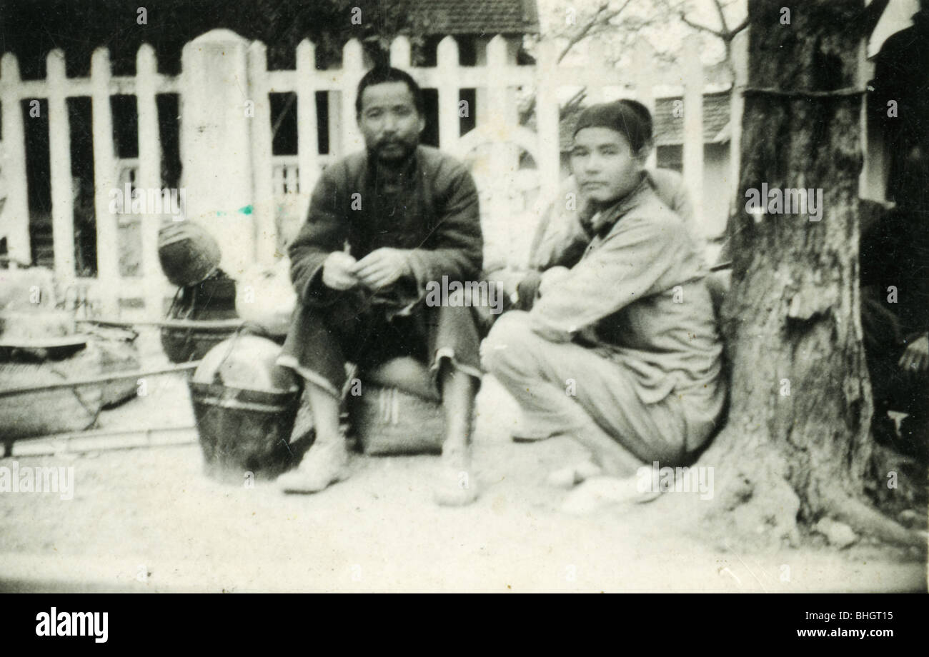 Vietnamita con baldes sentarse cerca de una valla blanca en una aldea de Vietnam. blanco y negro hombres machos horizontal Foto de stock