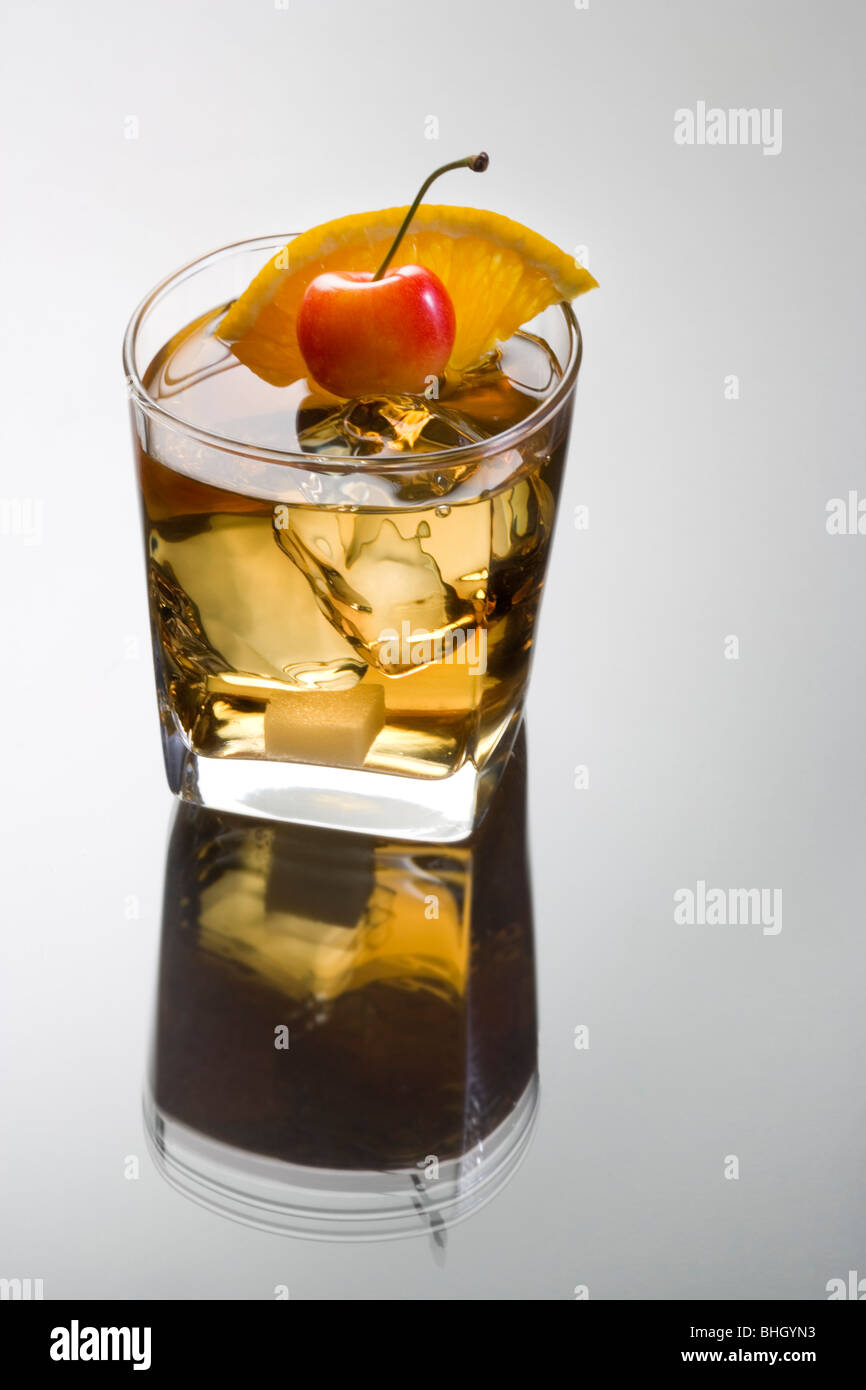 Antigua bebida mezclada con rodajas de naranja, cereza y Sugar Cube adorne sobre fondo gris con reflexión Foto de stock
