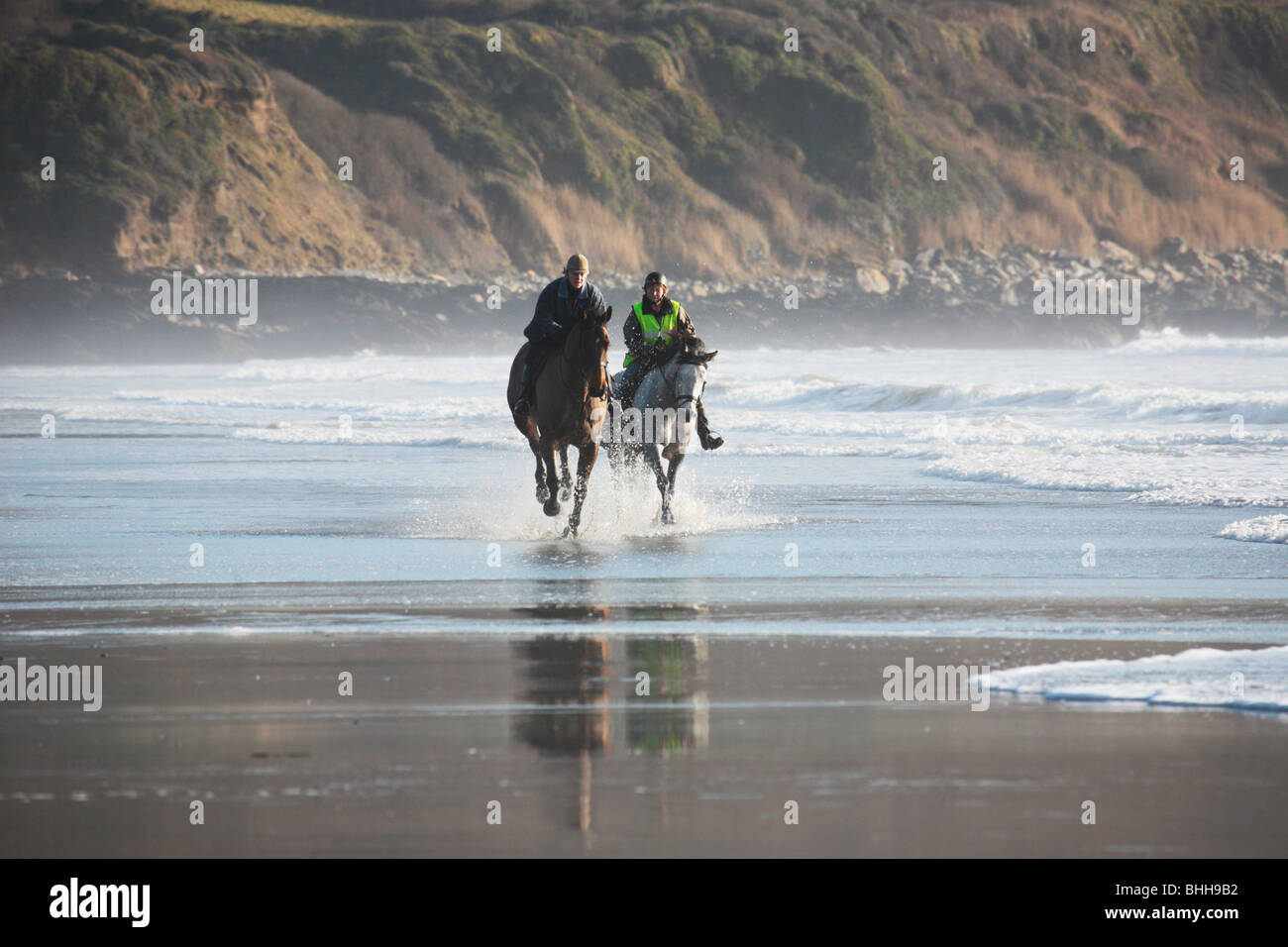 Playa Pendower, Cornwall, caballos galopando a través del surf con marea baja. Foto de stock