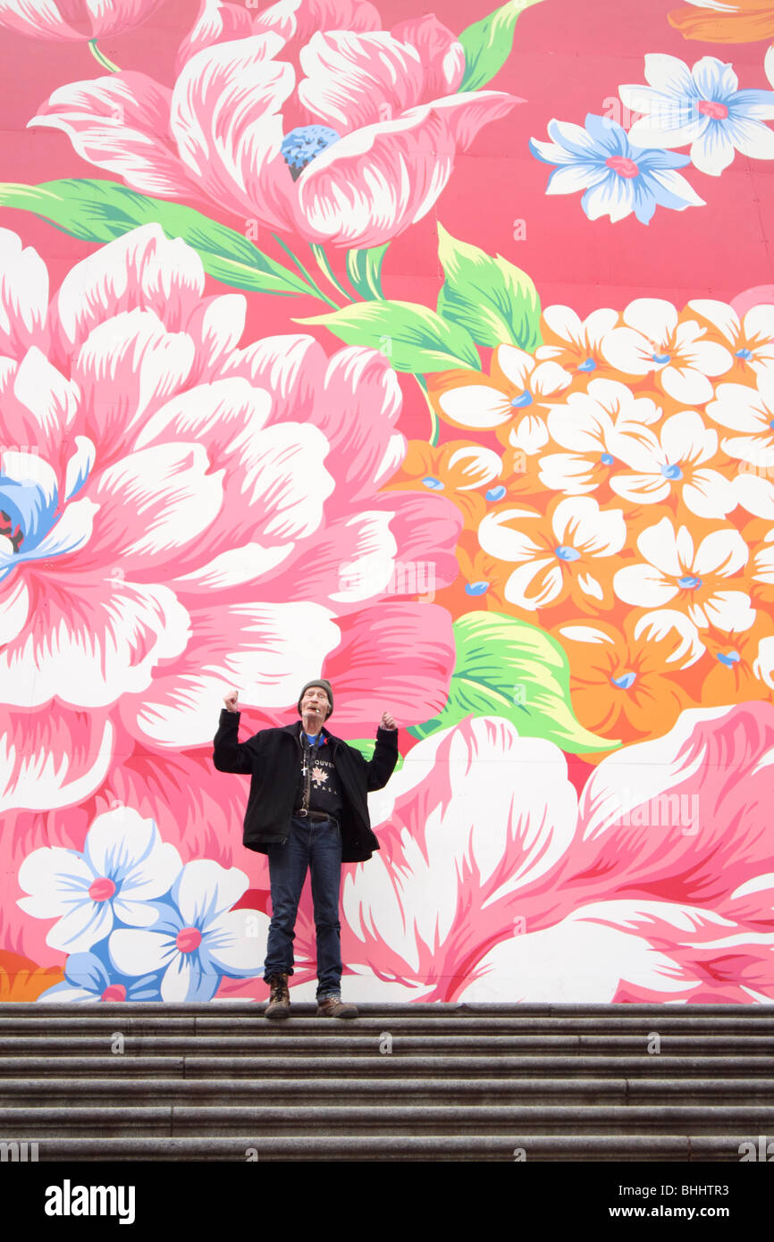 Personas sin hogar hombre de pie en los escalones en la parte delantera de la galería de arte de Vancouver con un patrón floral mural por Michael Lin. Foto de stock