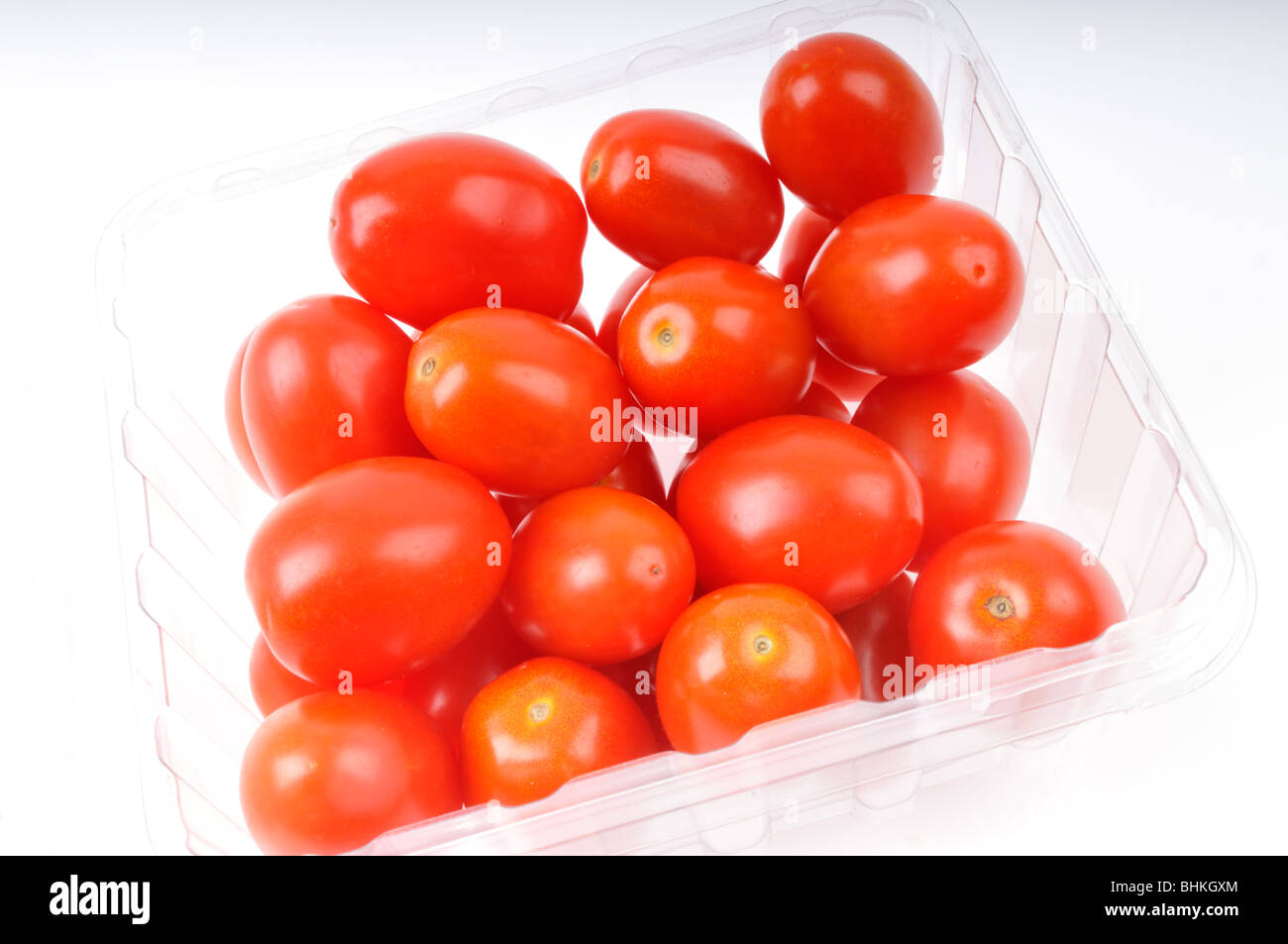 Tomates cherry rojos en el contenedor de plástico claro sobre fondo blanco. Foto de stock