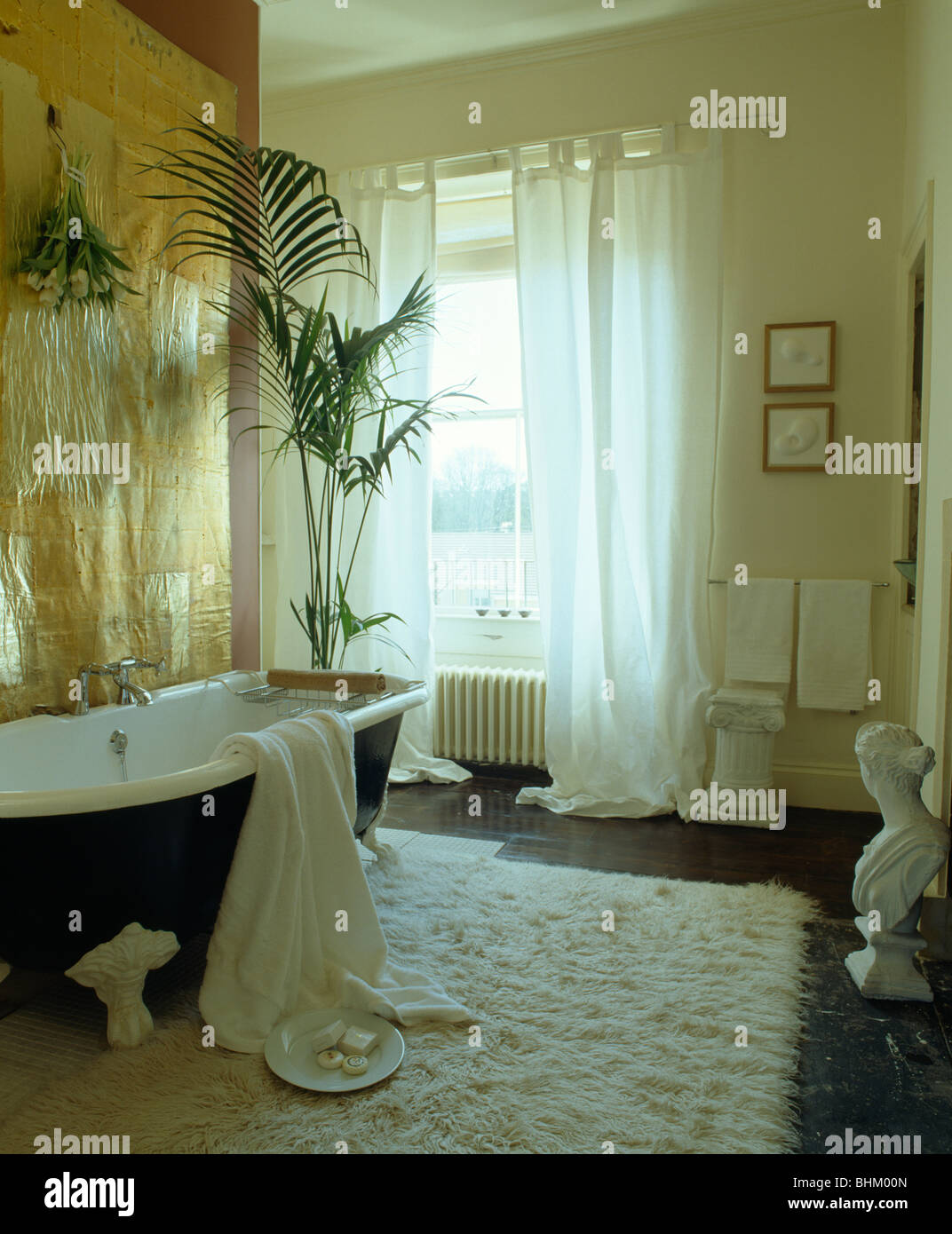 Panel dorado metálico encima del rodillo superior con bañera en el cuarto  de baño con ventana alfombras Flokati blanco con cortinas blancas  Fotografía de stock - Alamy