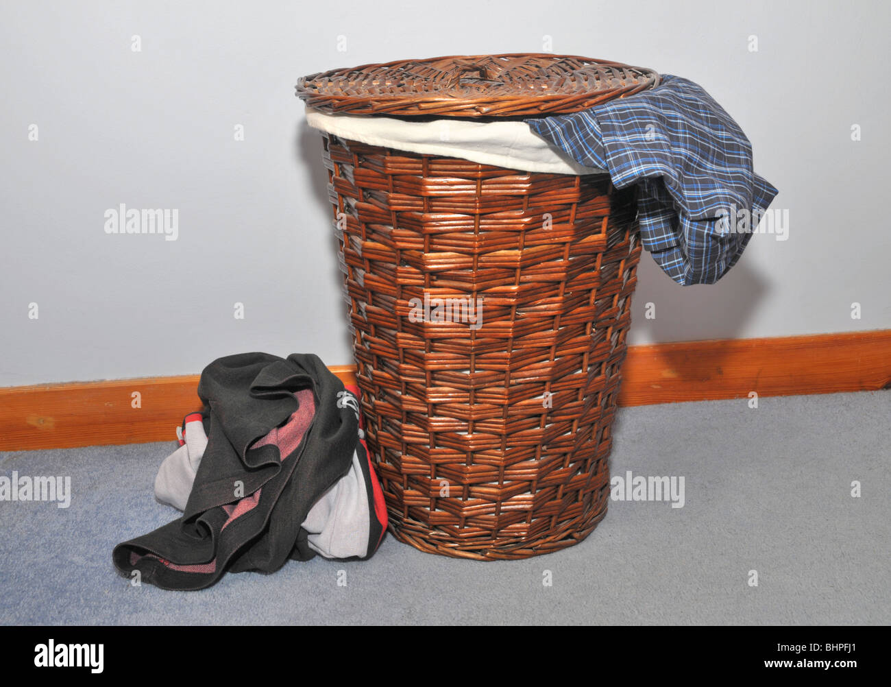 Una canasta de lavandería llena de ropa sucia se asienta sobre un piso de  madera.