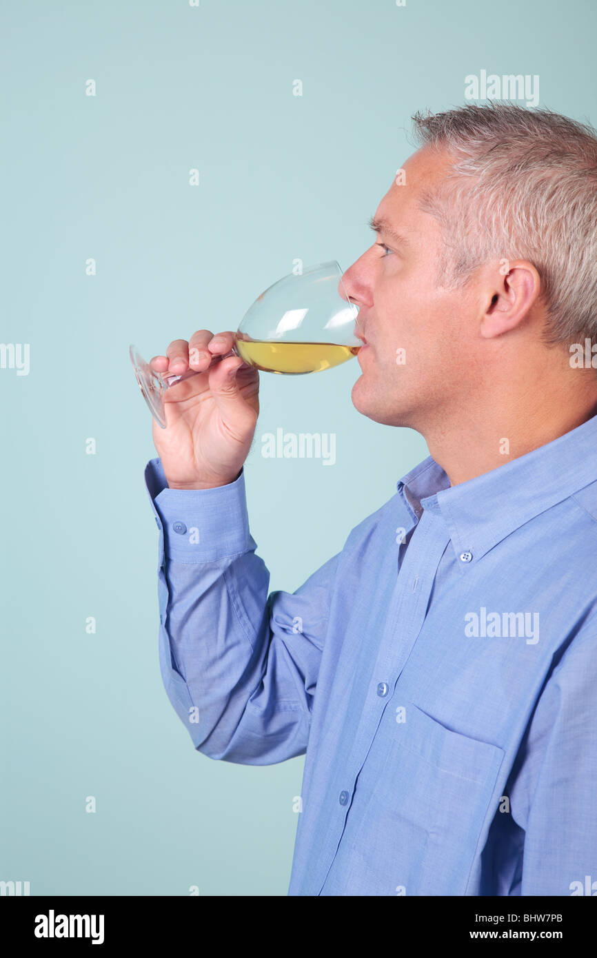 Hombre en una camisa azul beber un vaso de vino blanco Foto de stock