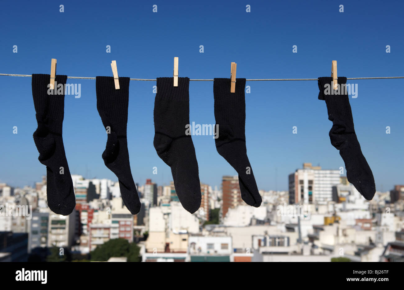 Cinco dos pares y una impar calcetines negros colgando de una línea de lavado con el cielo azul sobre una ciudad skyine en buenos aires argentina Foto de stock