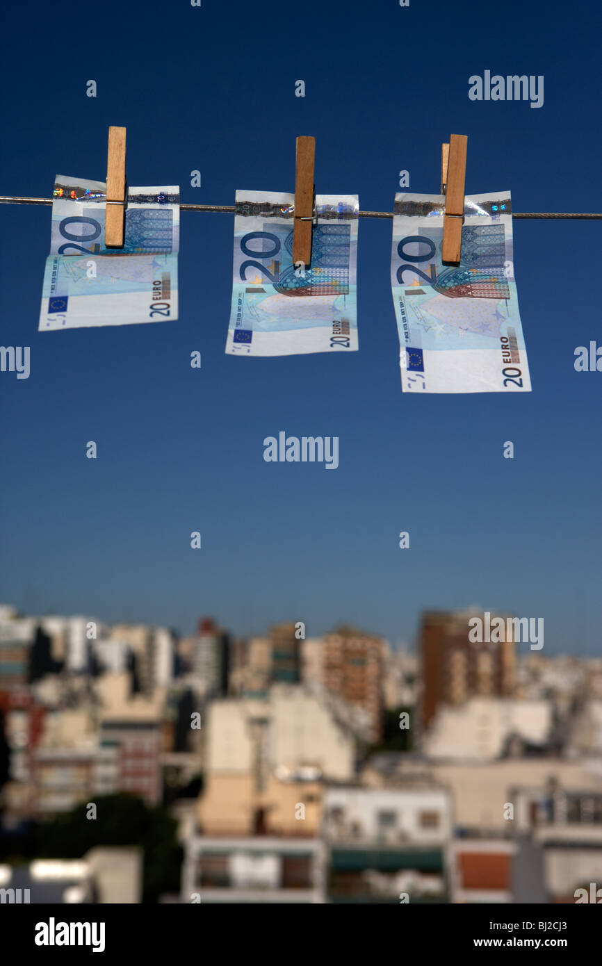 Tres veinte billetes colgando de una línea de lavado con el cielo azul sobre el horizonte de la ciudad Foto de stock