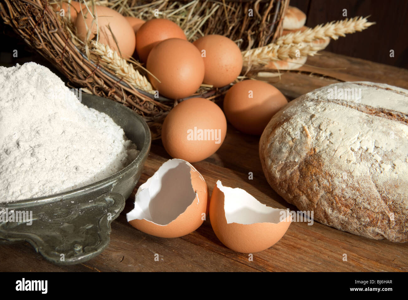 Los huevos en una canasta rústica con harina, panes y espigas de trigo