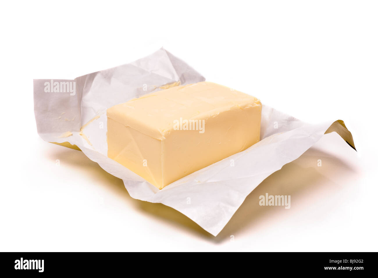 Trozo de mantequilla en papel sobre un fondo blanco. Enfoque superficial Foto de stock