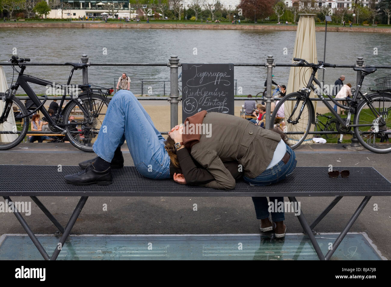 Pareja joven descansando sobre la banqueta moderna por el río con bicicletas Foto de stock