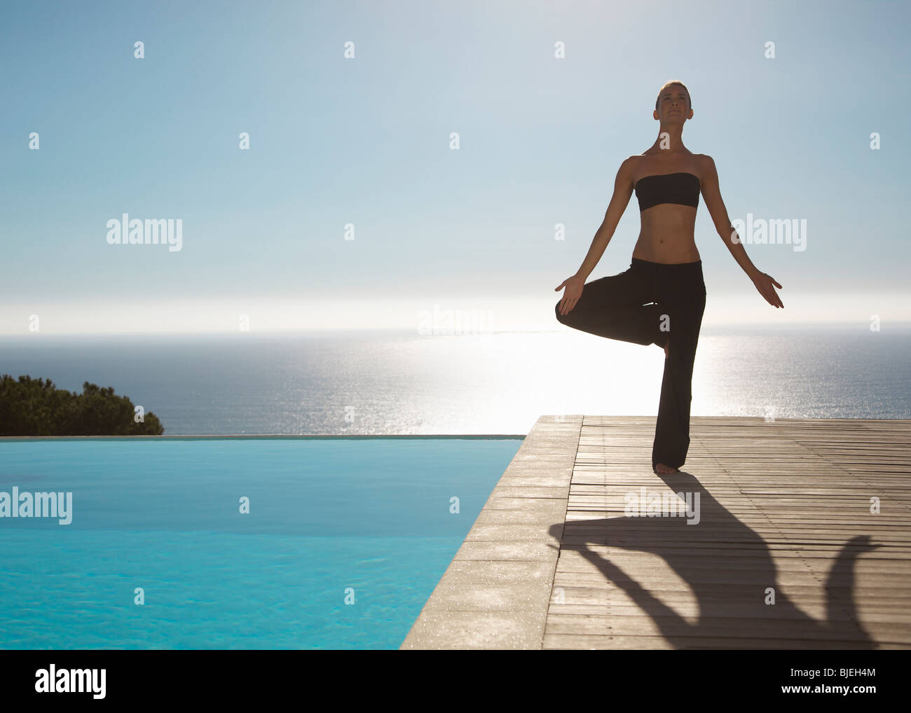 Mujer joven practicando yoga en una piscina con vistas al océano en el fondo Foto de stock