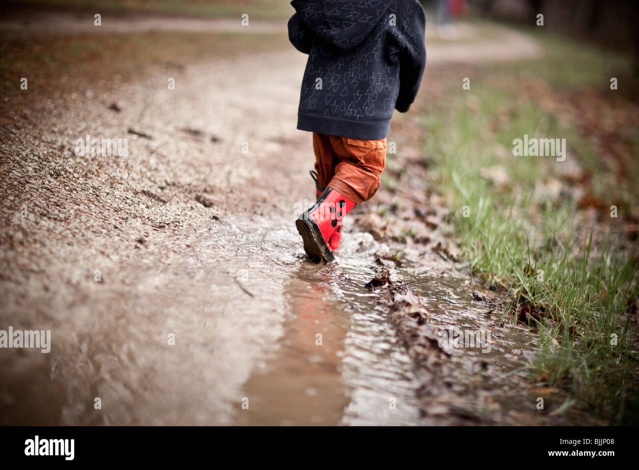 Joven llevaba botas de agua, camina a través de un charco de agua. Foto de stock