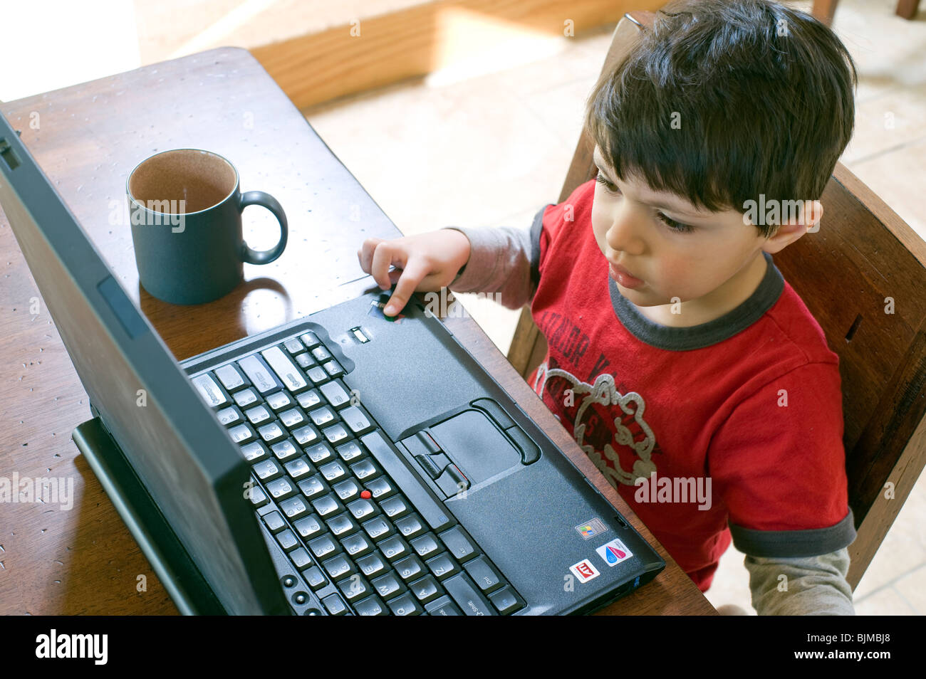 4 y 1/2 año viejo niño hispano navega por la web en su ordenador portátil de su mesa de la cocina. Modelo liberado. Foto de stock