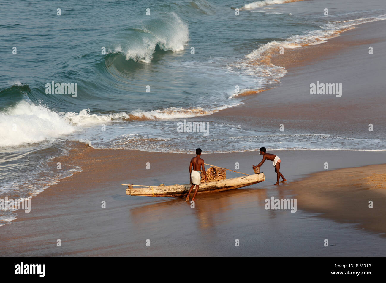 Dos locales con un simple barco de pesca en una playa al sur de Kovalam, la costa de Malabar, Malabar, Kerala, India del Sur, India, Asia Foto de stock