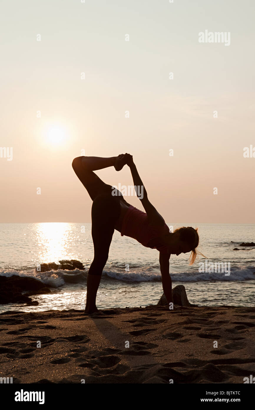 Mujer practicando yoga en una playa en el atardecer Fotografía de stock