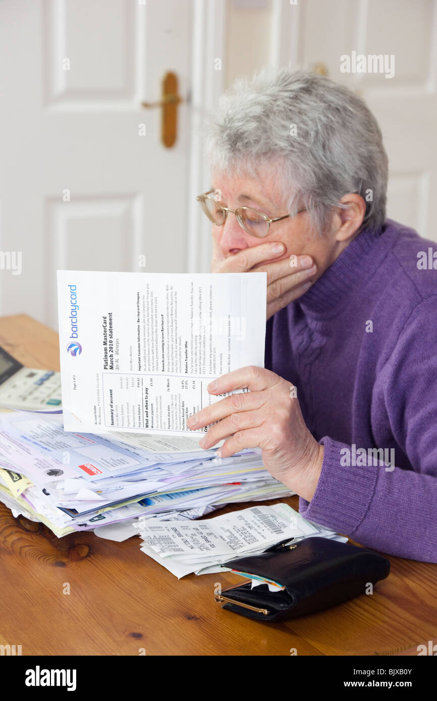 Conmocionado altos mujer pensionista jubilado con un montón de billetes con la mano sobre su boca buscando preocupados en un gran estado de tarjeta de crédito. UK Foto de stock