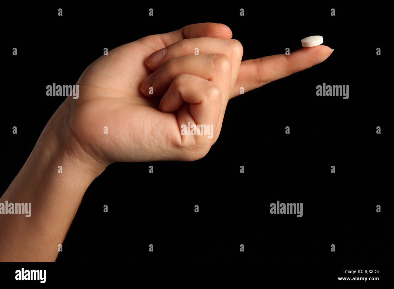 Una mano femenina sosteniendo una pequeña pastilla blanca entre los dedos Foto de stock