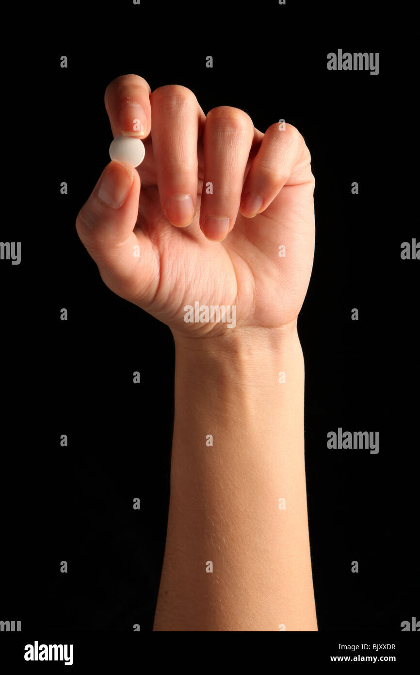 Una mano femenina sosteniendo una pequeña pastilla blanca entre los dedos Foto de stock