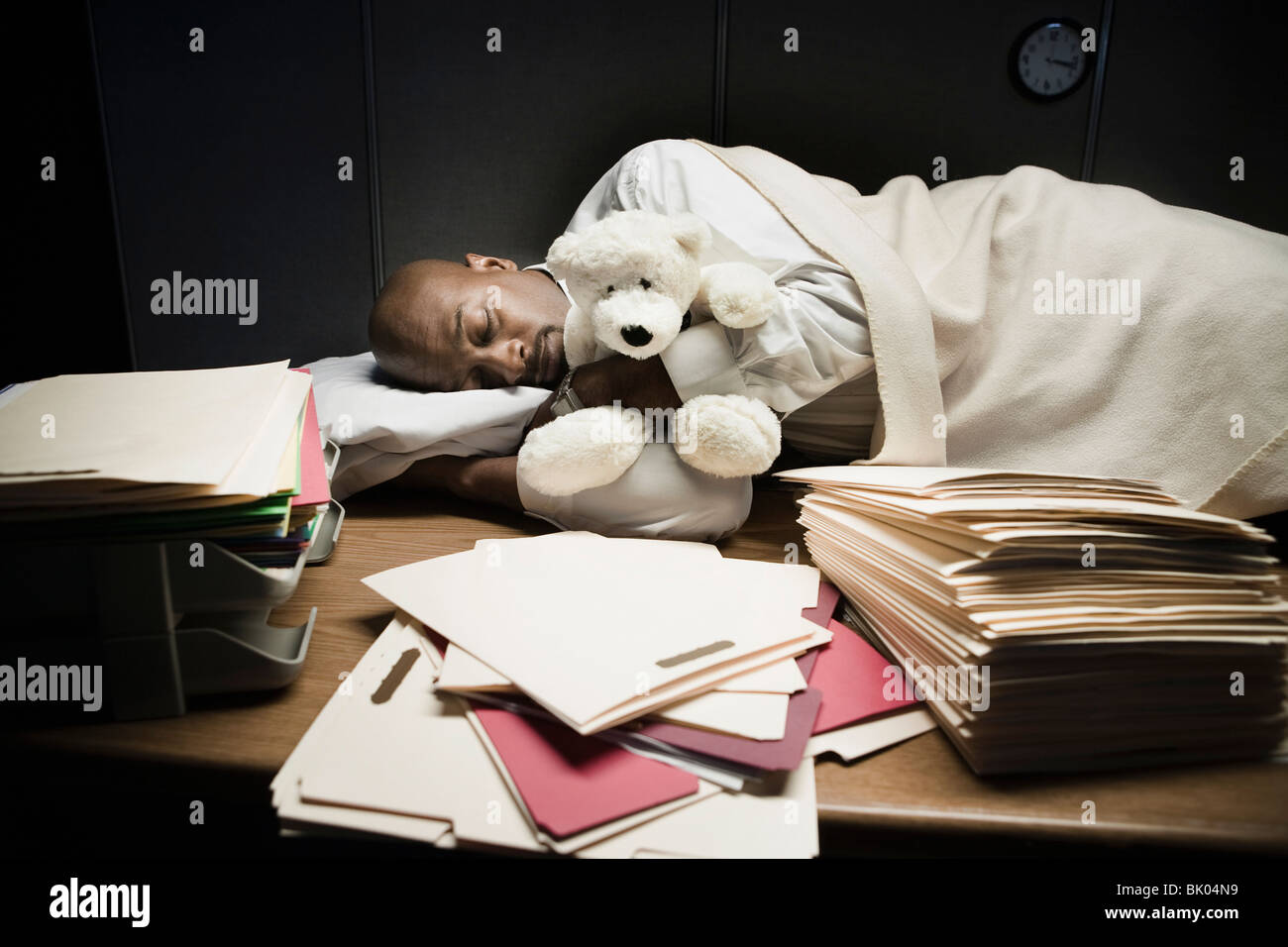 Hombre con animal de peluche durmiendo en el escritorio Foto de stock