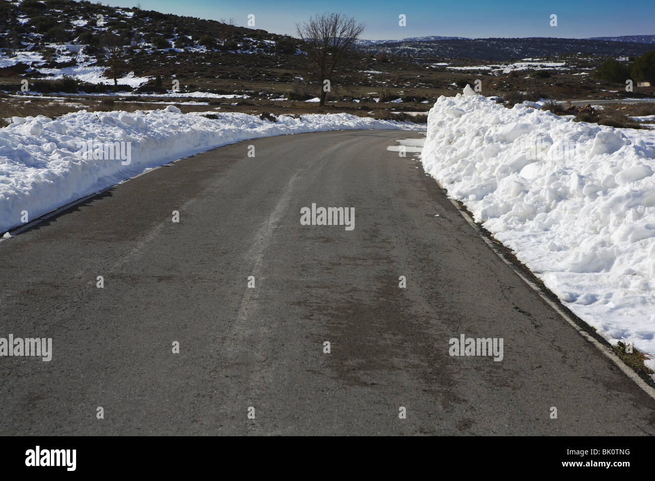 Curva de asfalto con nieve en ambos lados de las fronteras Foto de stock