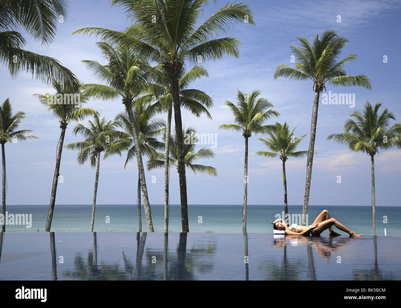 Mujer joven relajándose en la piscina con palmeras y el mar Foto de stock