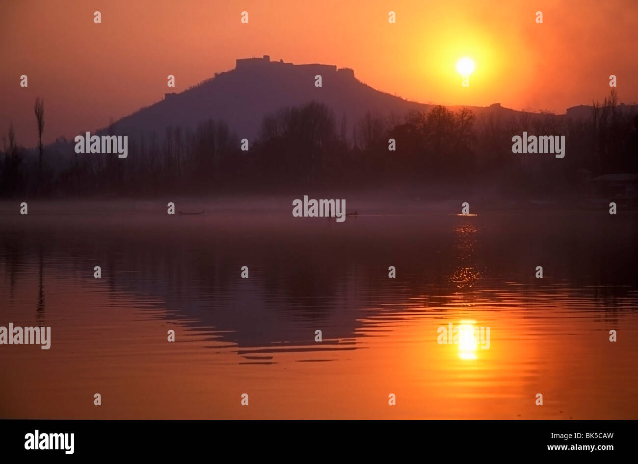 Los pescadores hacen su camino a casa en canoas como puestas de sol sobre el lago Nigeen, Srinagar, capital de la Cachemira administrada por India, India Foto de stock