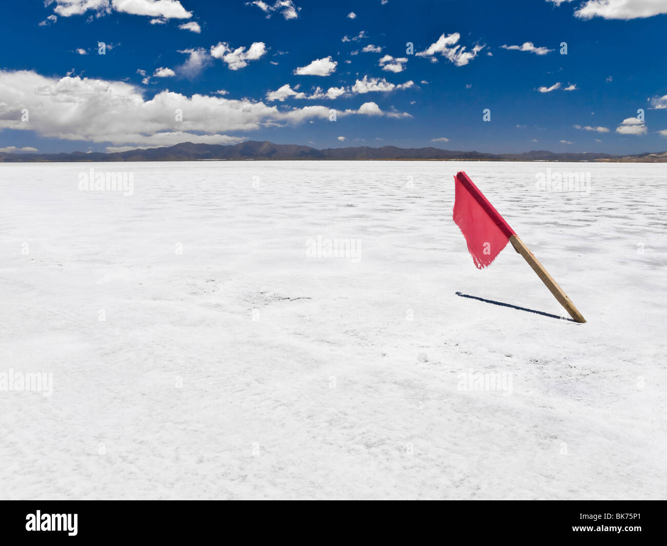 Una bandera roja pegada en un enorme campo de sal. Foto de stock