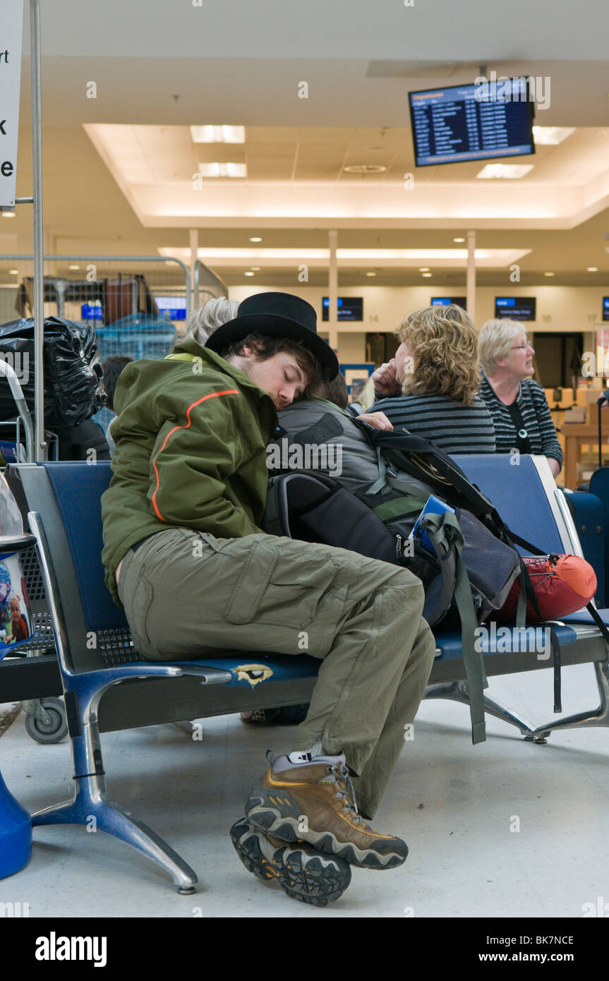 Hombre durmiendo en un aeropuerto sentado mientras es vuelo es cancelado Foto de stock