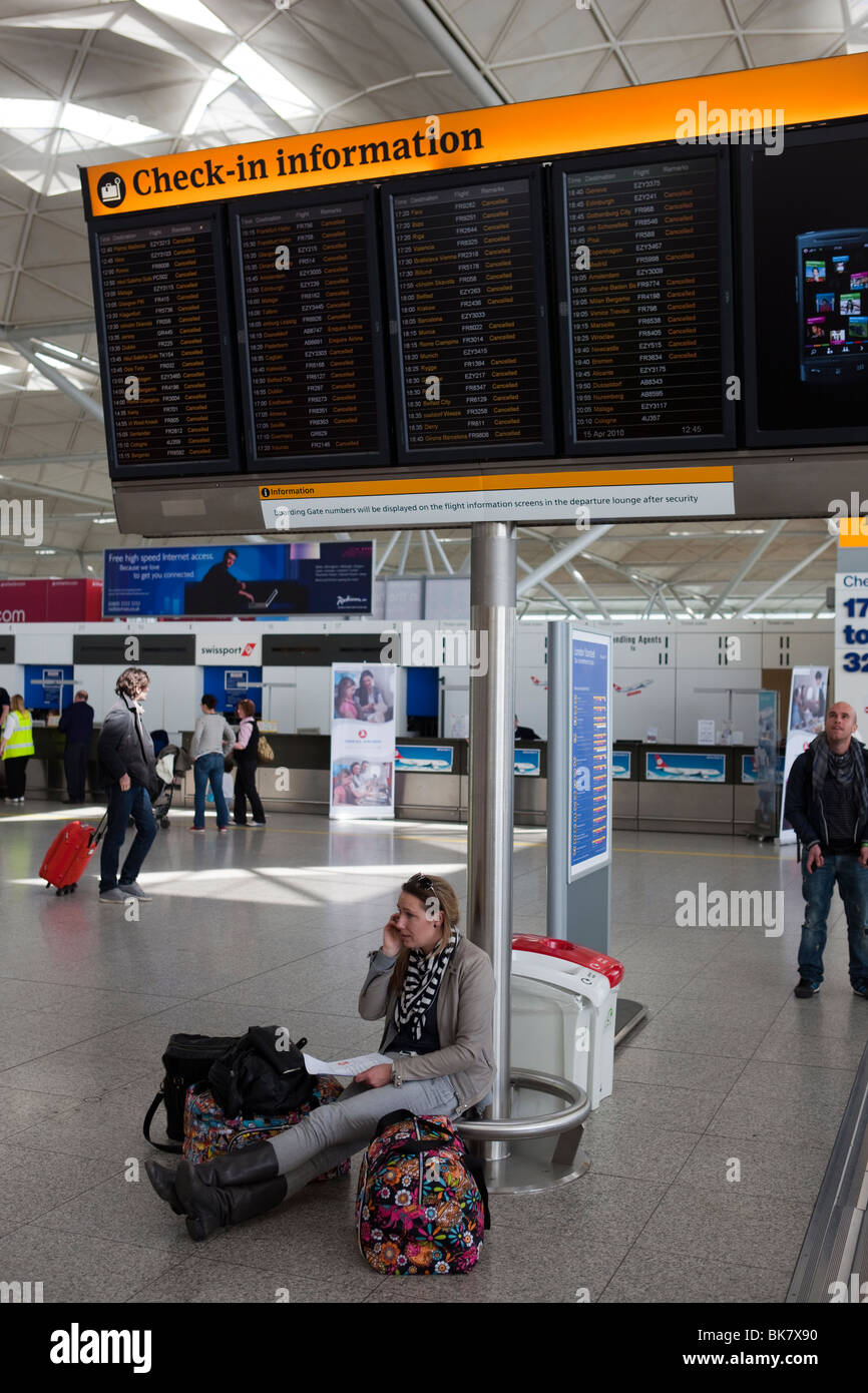 Un pasajero se sienta debajo de un aeropuerto check-in information board mostrando todos los vuelos cancelados hablando por su teléfono móvil Foto de stock