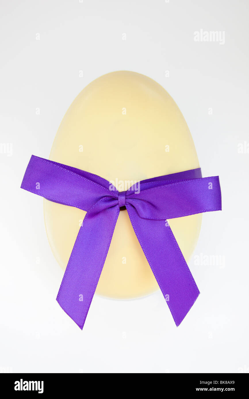 Huevo de Pascua de chocolate blanco morado con un lazo atado en un arco. Foto de stock