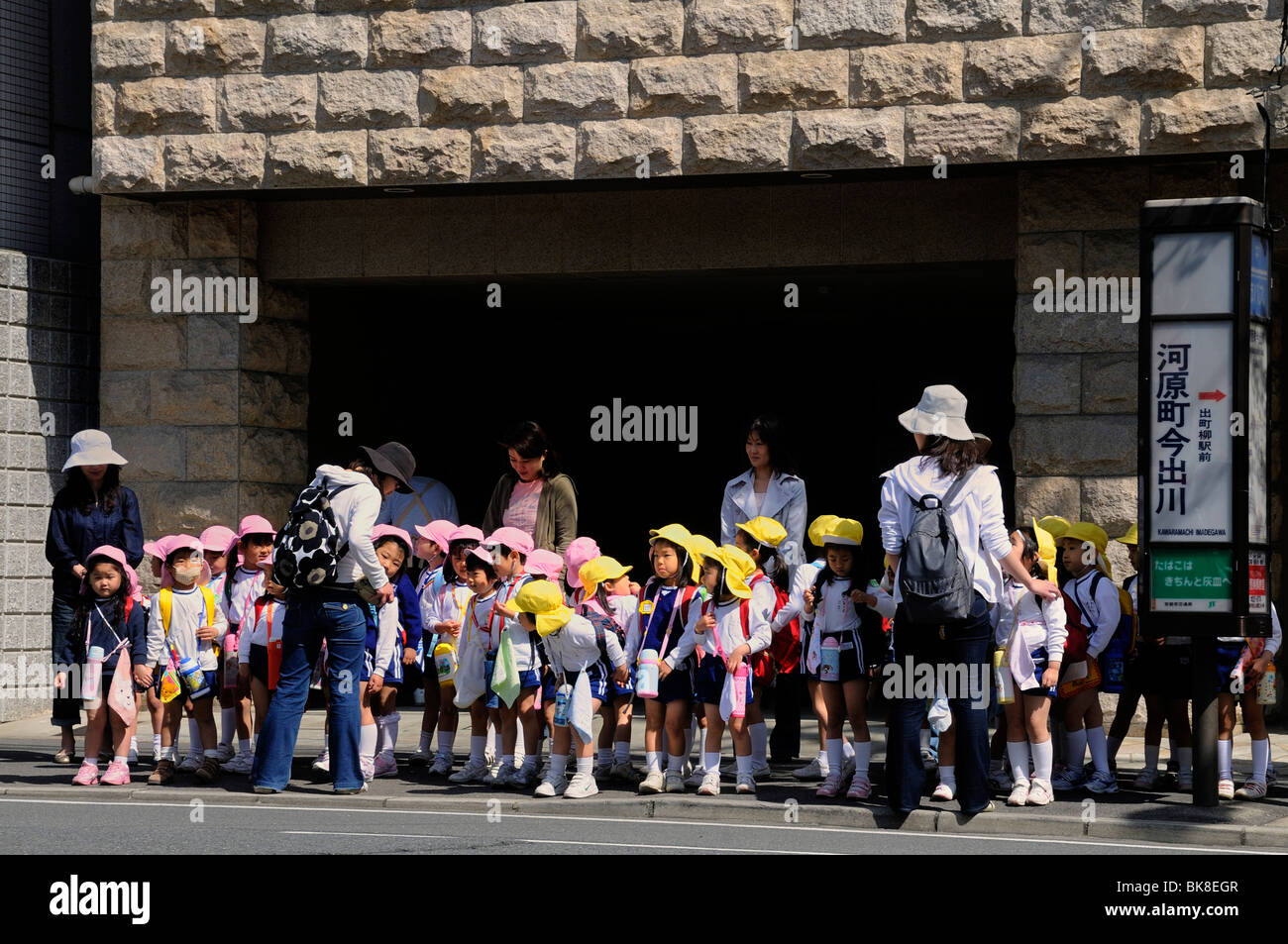 Los niños, las niñas y los niños con amarillo y rosa con tapas, esperando en el centro de la ciudad de autobús, Kyoto, Japón, Asia Foto de stock
