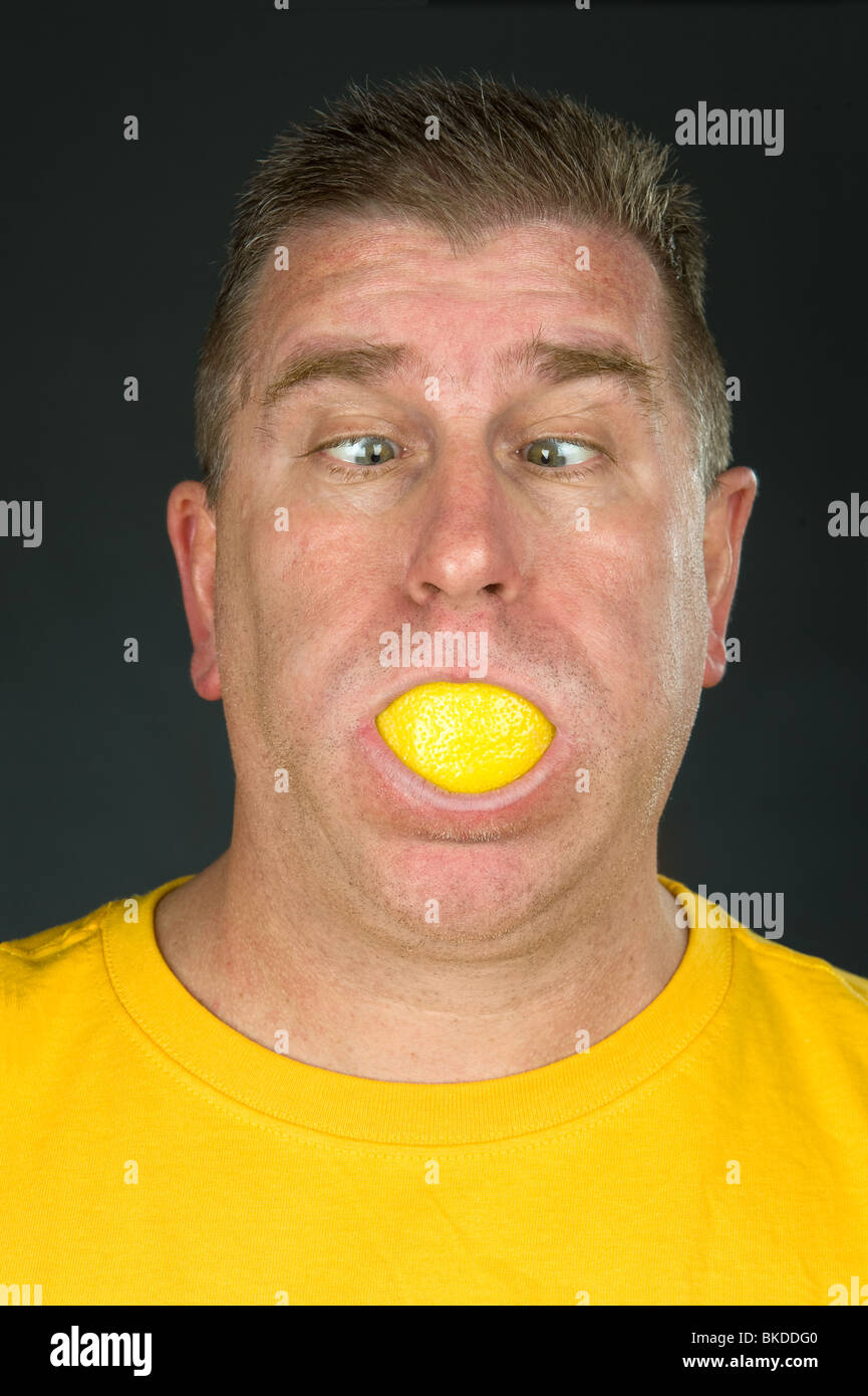 Un hombre aspira a una rodaja de limón agrio y hace una cara divertida debido al sabor agrio. Foto de stock