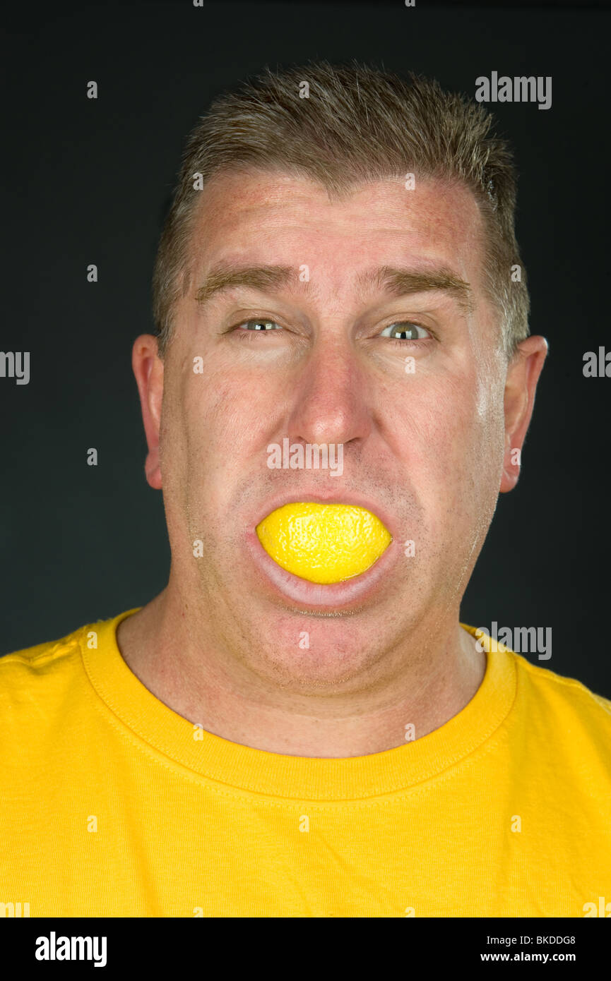 Un hombre chupa un limón como se mira de reojo y irregularidad con el amargo sabor agrio. Foto de stock