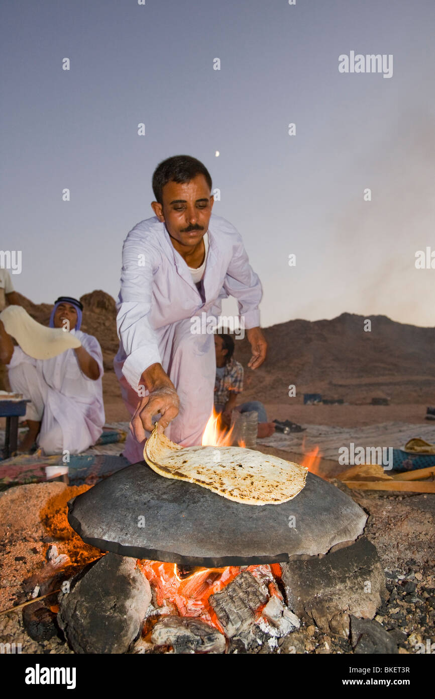 Un hombre beduino cociendo pan en un fuego abierto en un campamento en el desierto del Sinaí, cerca de Dahab en Egipto Foto de stock